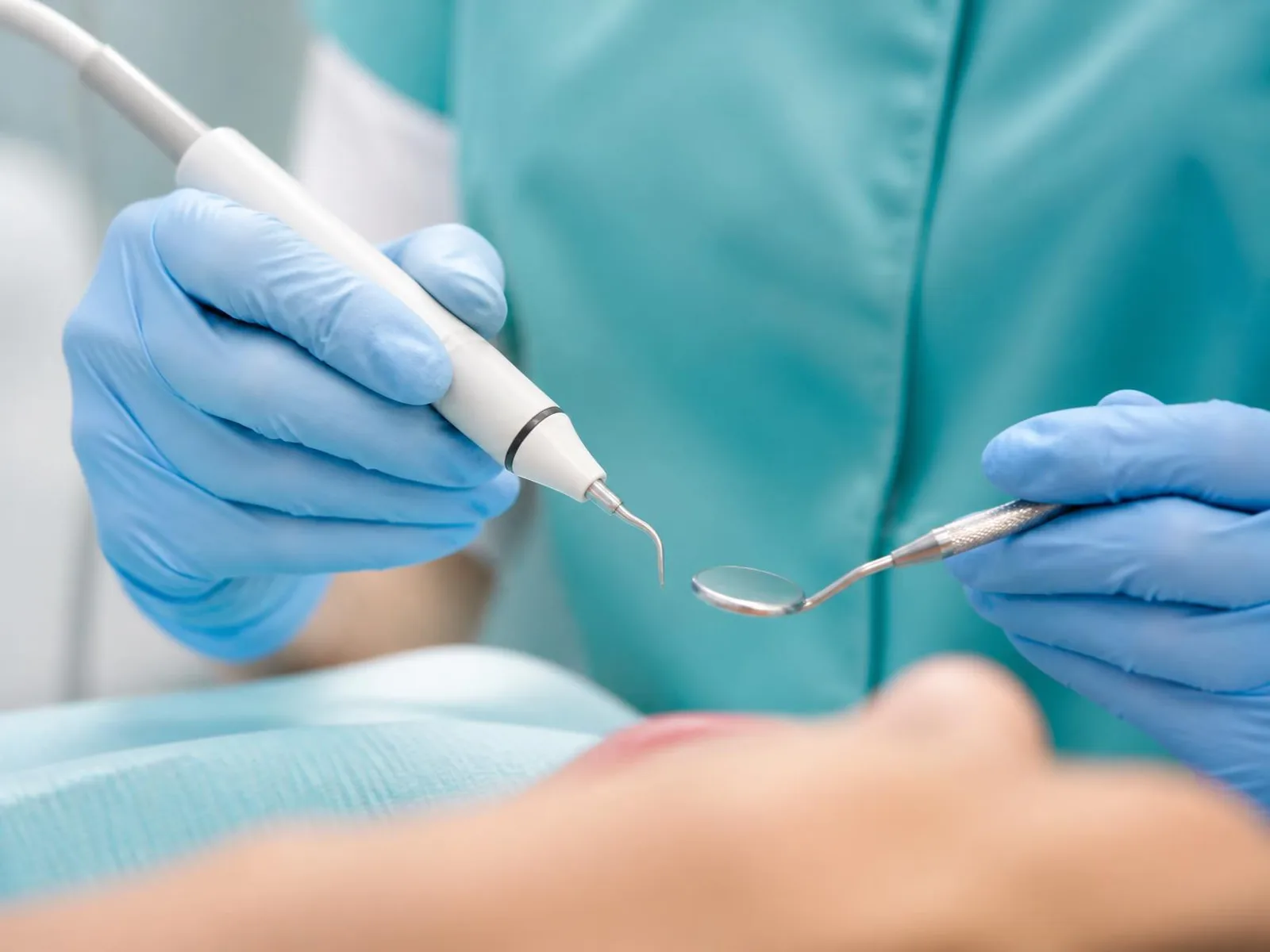 Ruky v rukaviciach držia ultrazvukový nástroj a zubné zrkadielko